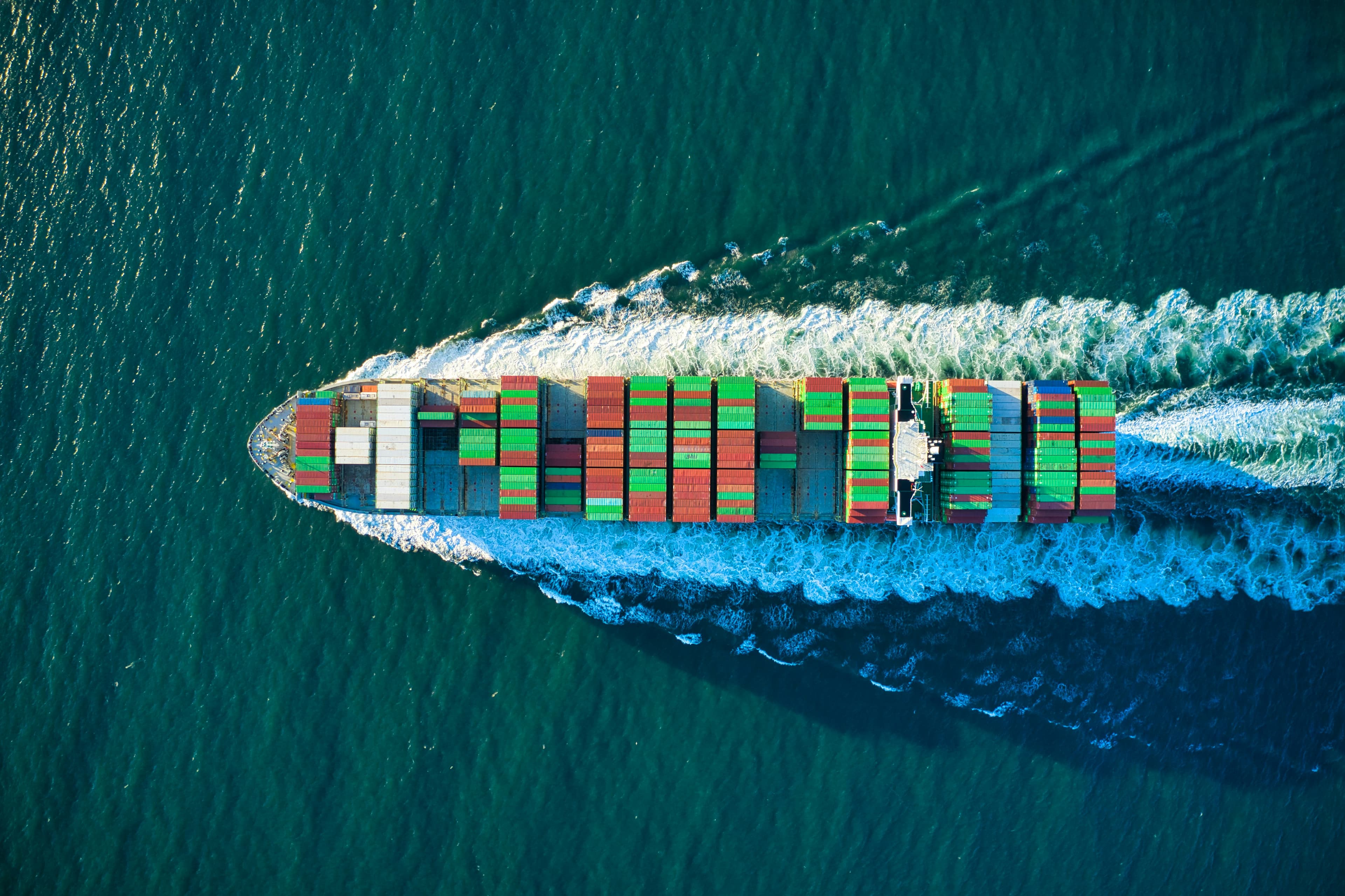 Aerial view of a loaded container ship underway, wake trailing behind